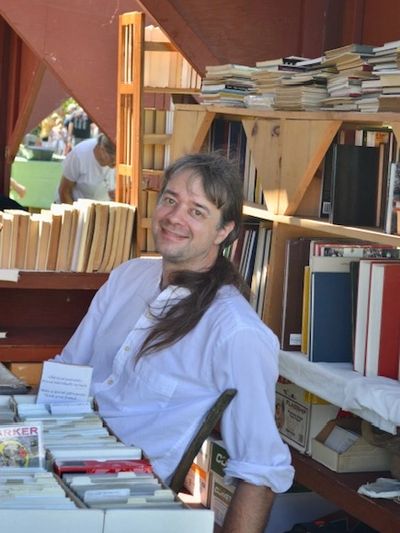 Smiling man in white shirt at a bookstall filled with books.