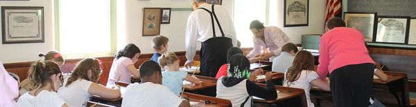 Children in a classroom with two teachers assisting them.