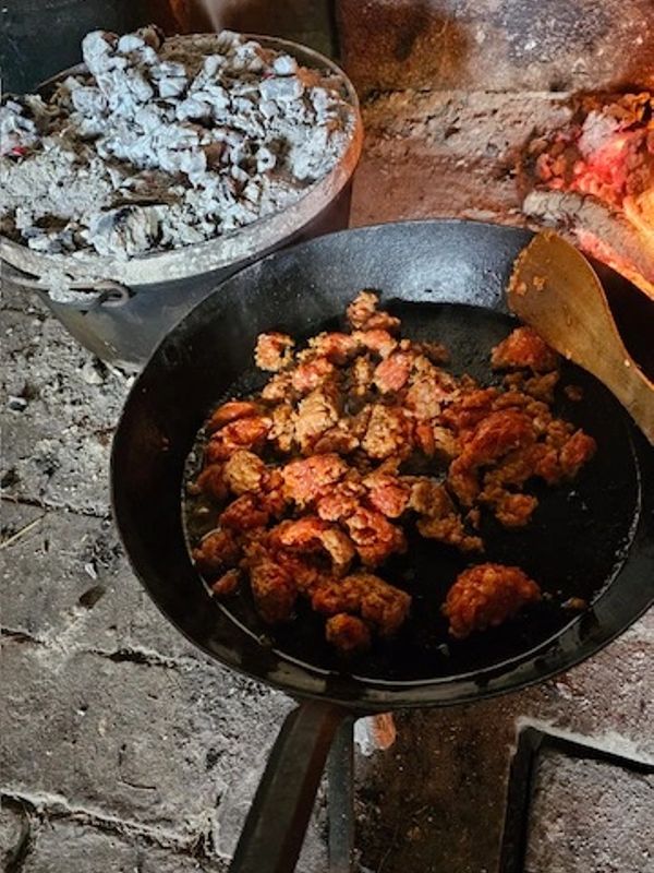 Old-fashioned frying pan cooking meat over a wood fire stove.