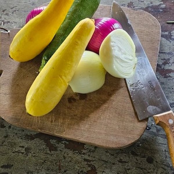 Yellow squash, zucchini, and onions on a wooden cutting board with a knife.