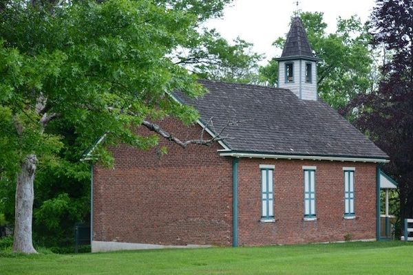 Small brick church with steeple surrounded by green trees and grass.