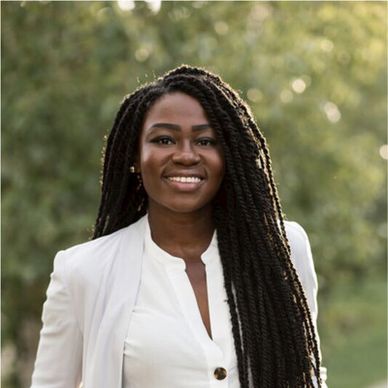 Smiling woman with long braided hair in a white outfit outdoors.
