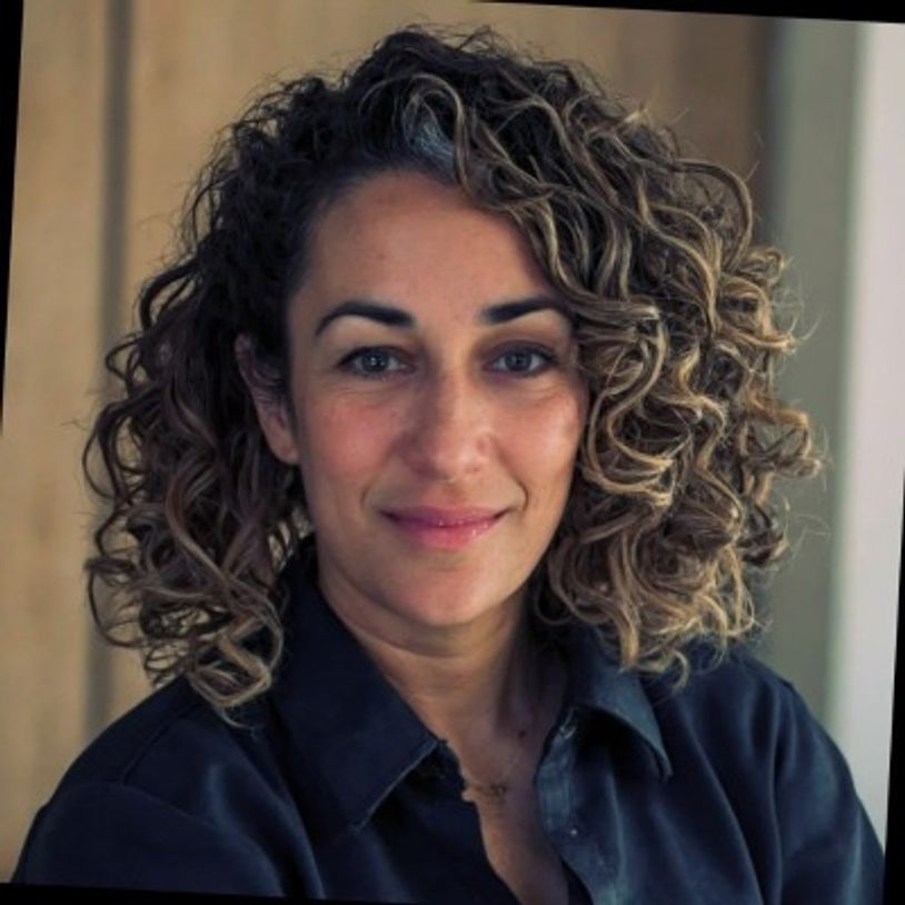 Woman with curly hair and a gentle smile wearing a dark shirt.