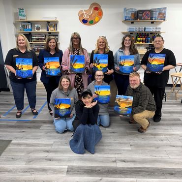 Group of people holding sunset paintings in art studio.