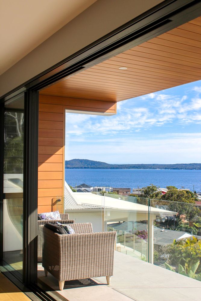Cozy balcony with wicker chairs overlooking a serene ocean and distant hills / Custom Home Building