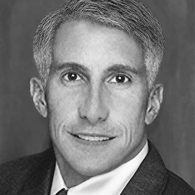 Black and white headshot of a man in a suit smiling.