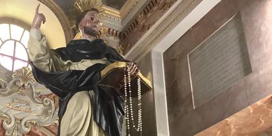 Statue of a saint holding a rosary inside a church.