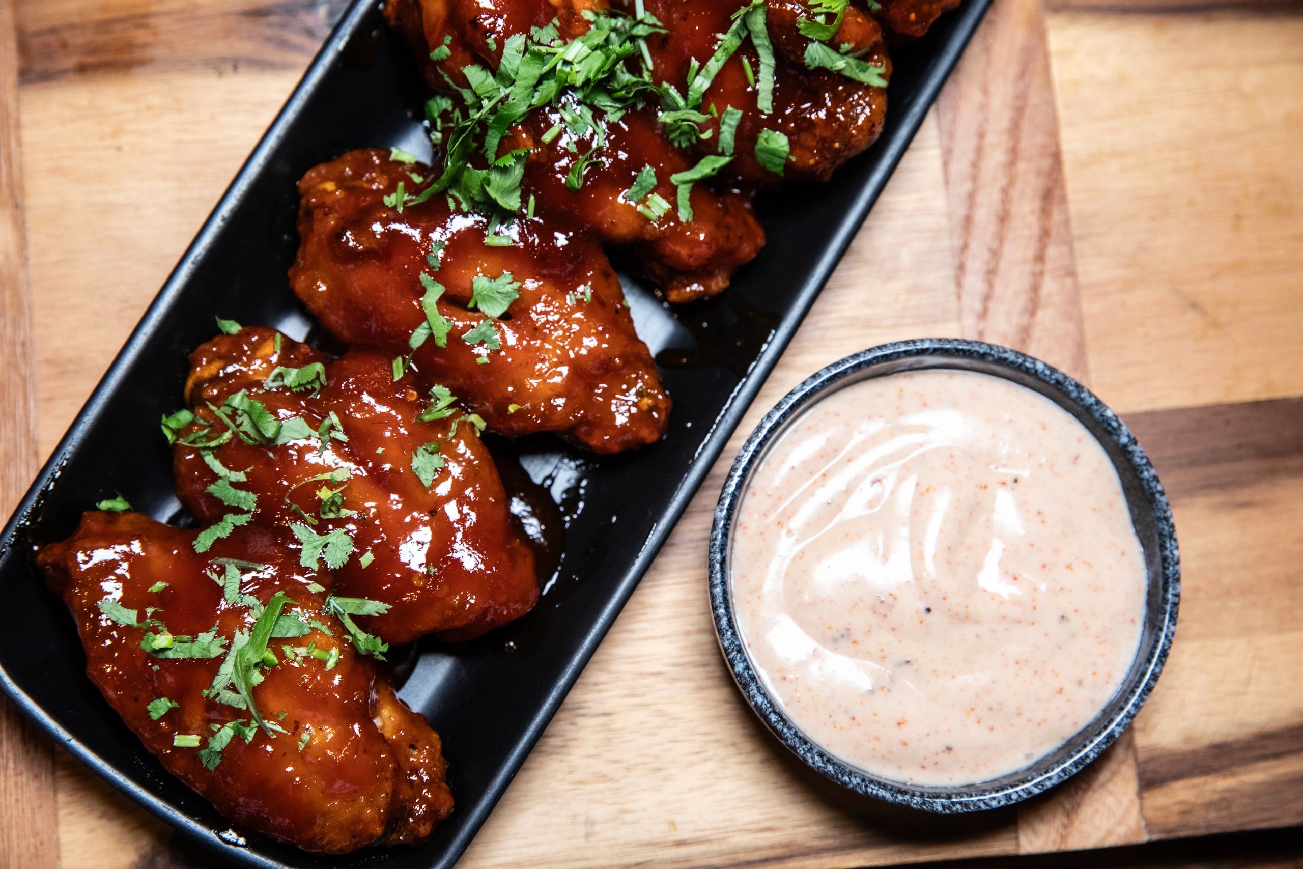 Buffalo wings with sauce and a creamy dip on a wooden board.