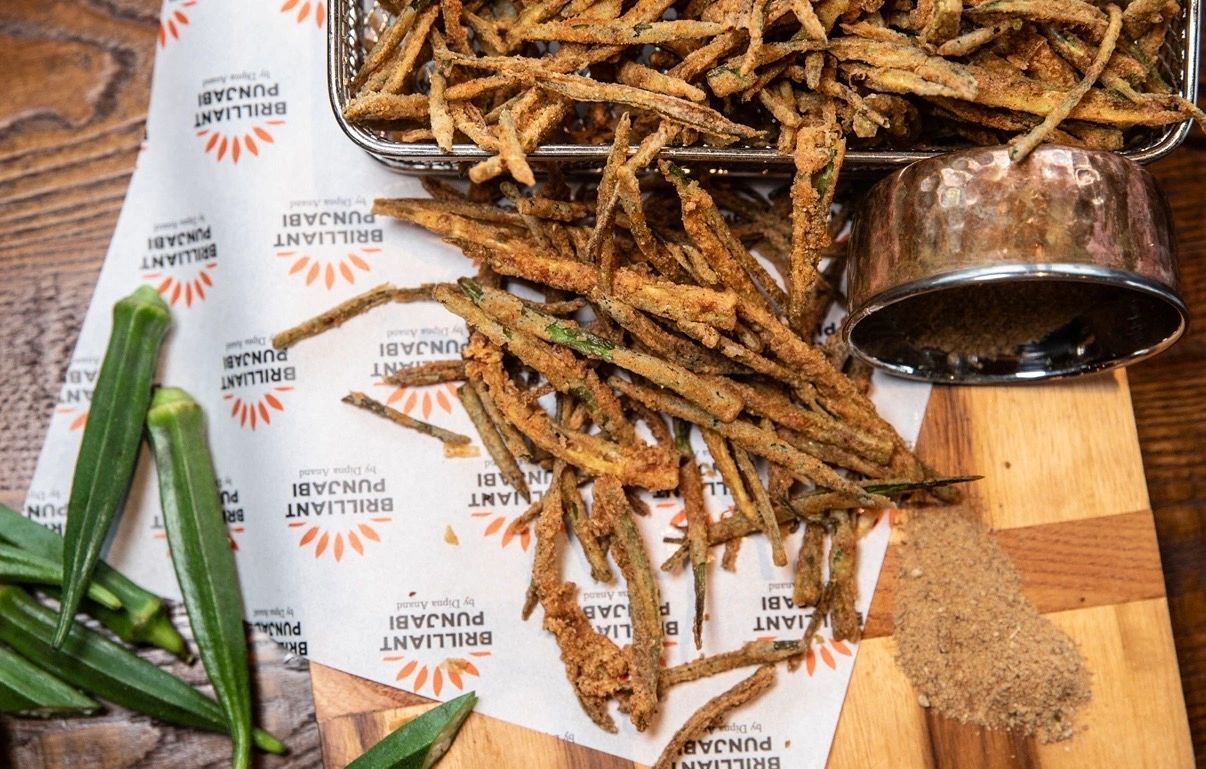Fried okra sticks served with seasoning on a wooden board.