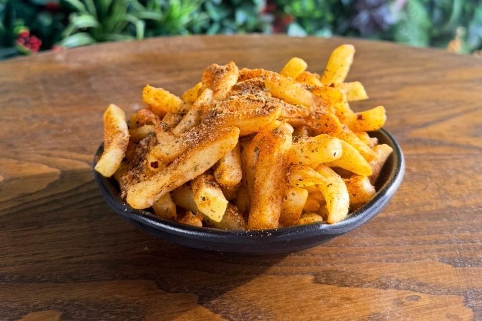Bowl of seasoned French fries on a wooden table.