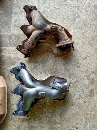 Two car exhaust manifolds, one worn and rusty, one clean and new.