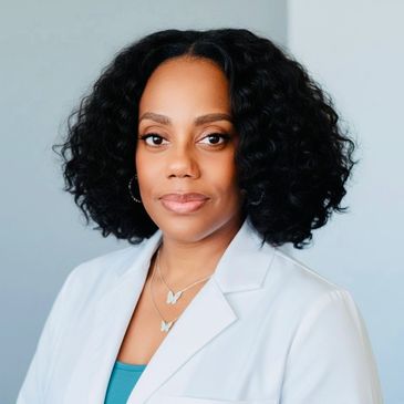 A female trichologist in a white lab coat with natural shoulder-length curls.