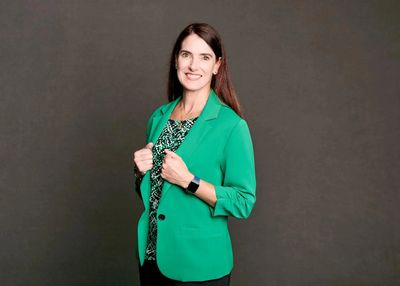 Woman in green blazer smiling against a dark background.