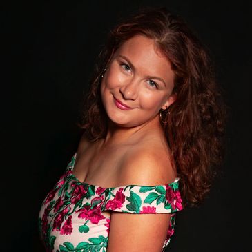 Young woman in a floral off-shoulder dress posing against a black background.