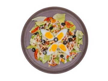 Fresh salad with boiled eggs, olives, tomatoes, lettuce, and dressing on a gray plate.