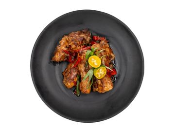 Grilled chicken wings garnished with sliced calamansi and chili peppers on a black plate.