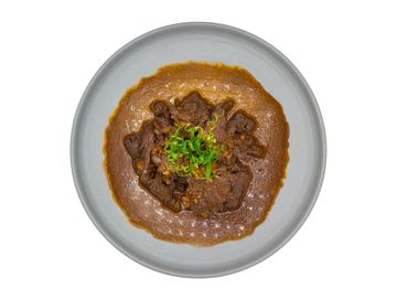 A plate of beef stew garnished with green onions and surrounded by rich brown gravy.