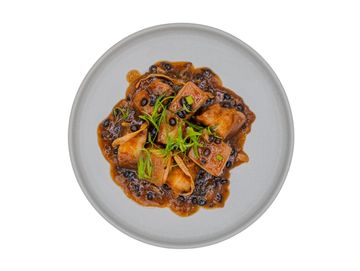 Braised tofu in black bean sauce garnished with green onions on a gray plate.