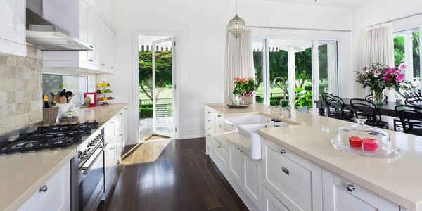 Bright modern kitchen with white cabinets, dark wood flooring, and a view of greenery outside.