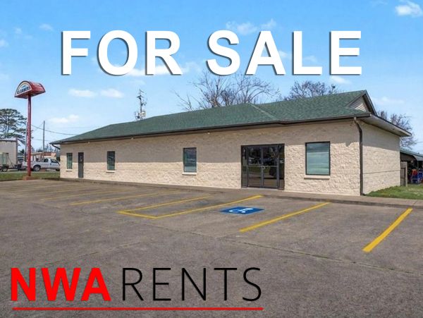 Commercial building with 'FOR SALE' sign and parking space.