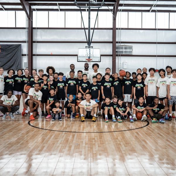 Large diverse group of kids and adults posing on basketball court.