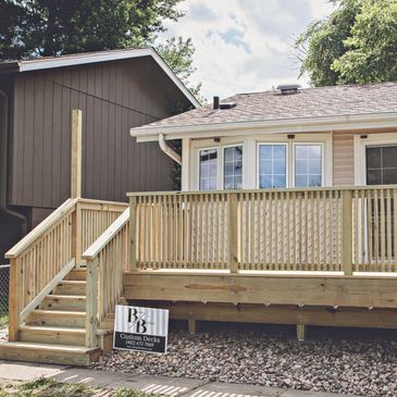 New wooden deck with stairs and railing attached to a house.