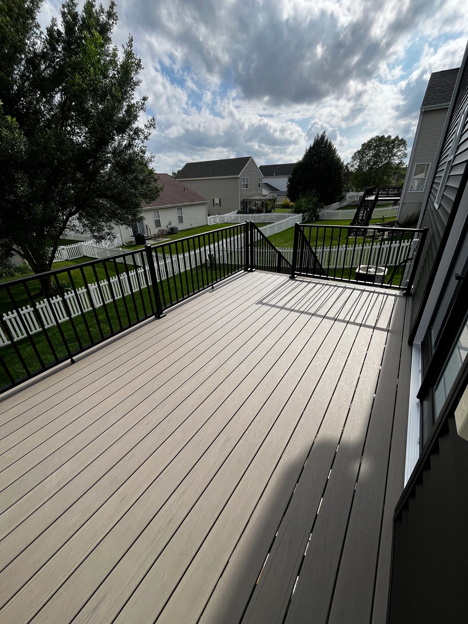 Sunny backyard deck with black railing and white fences.