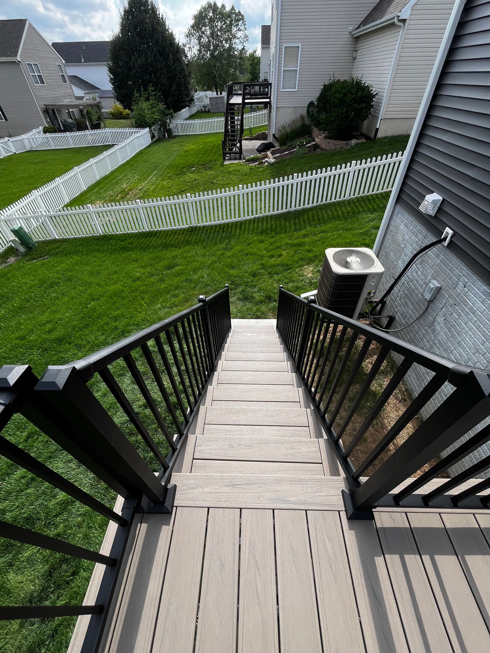 View down a staircase to a green backyard with white fences.