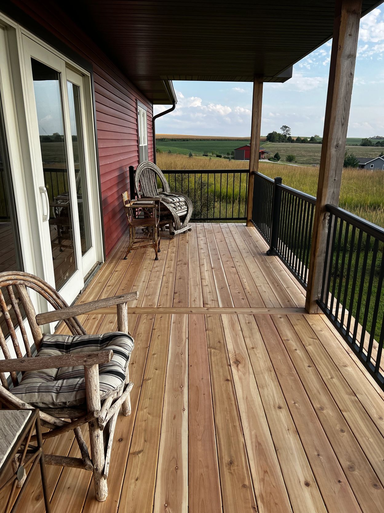 Wooden porch with rustic chairs overlooking fields.