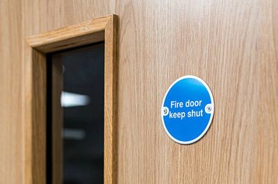 Close-up of a wooden fire door with a blue 'Fire door keep shut' sign.