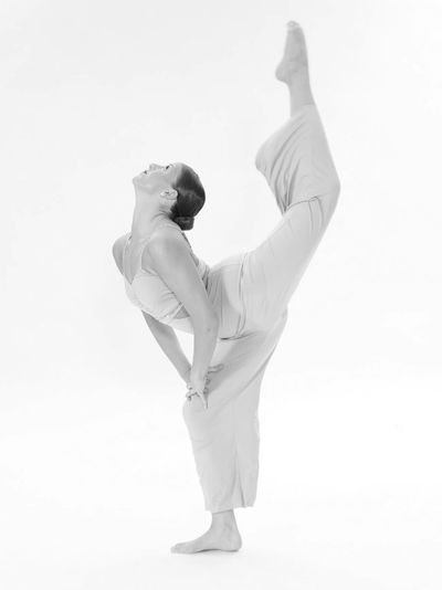 Woman performing a high leg stretch in beige outfit.