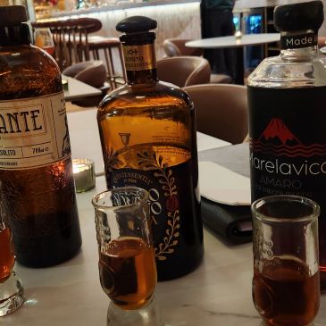 Three bottles of amaro with three filled shot glasses on a restaurant table.