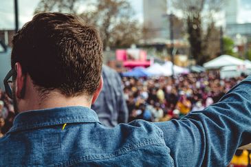 Camera shot behind the should of a man on stage looking into the crowd