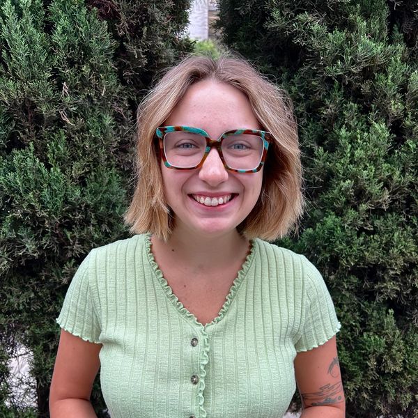 Smiling woman with glasses in green top against greenery.