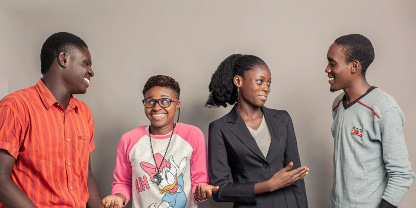 Four people smiling and interacting against a plain backdrop.