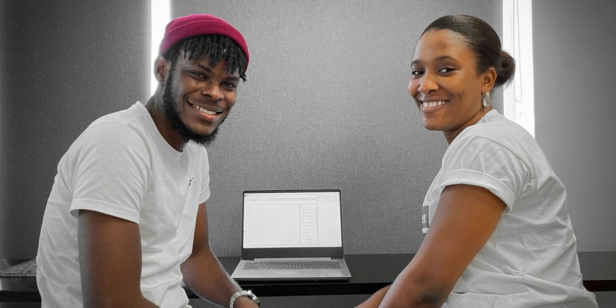 Two young adults smiling near a laptop.