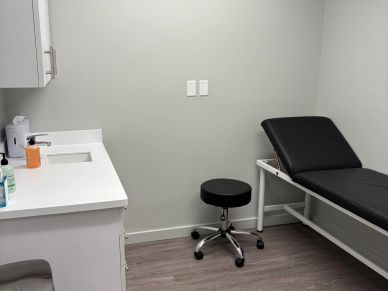 A clean, minimal medical examination room with a black examination table and stool.