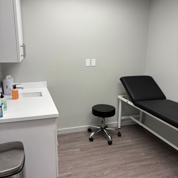 A clean, minimal medical examination room with a black examination table and stool.