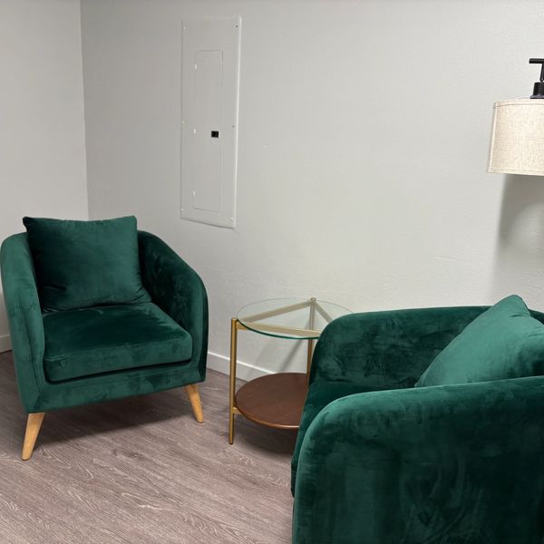 Two green velvet armchairs with wooden legs and a glass-top side table between them.