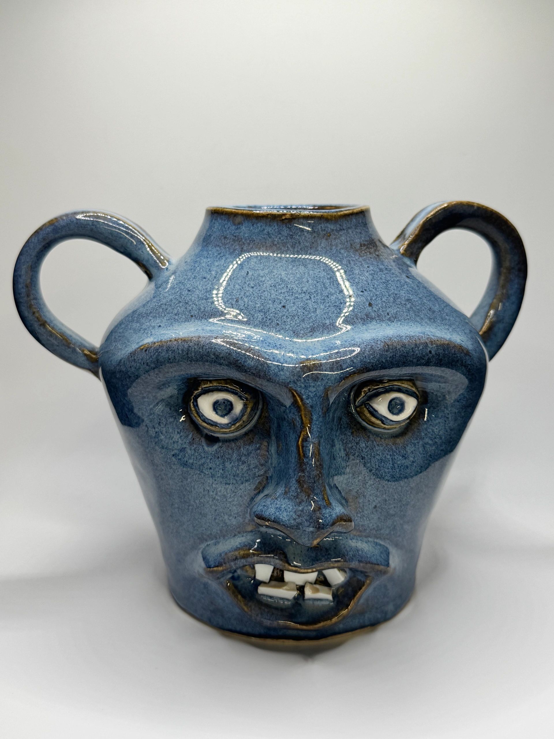 Blue ceramic face jug with two handles and white teeth.