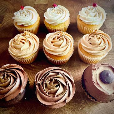 Nine assorted frosted cupcakes on a wooden surface.