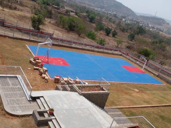 An outdoor basketball court with blue and red markings in a dry, hilly area.