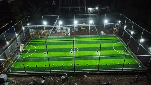 Illuminated mini soccer field enclosed with netting at night.