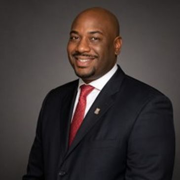 Professional man in a dark suit with a red tie smiling.