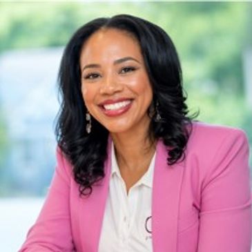 Smiling woman in a pink blazer posing indoors.