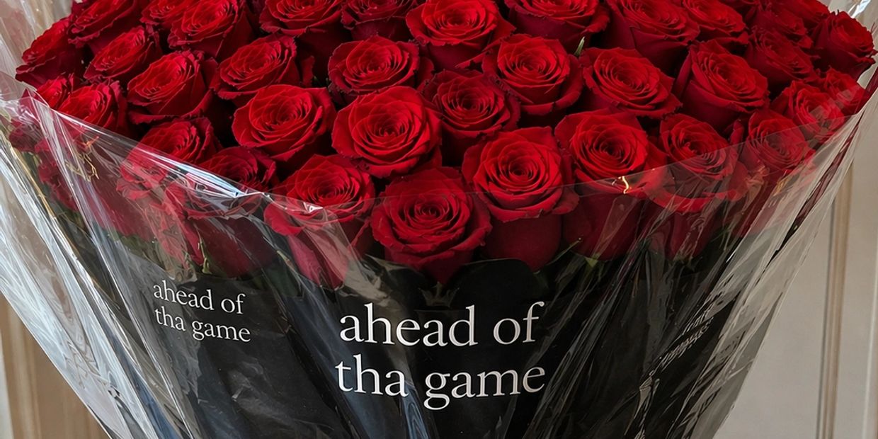 A bouquet of vibrant red roses wrapped in plastic with the phrase 'ahead of tha game'.