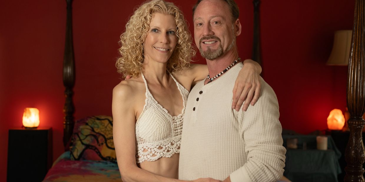 Smiling couple embracing in a warmly lit bedroom with red walls.