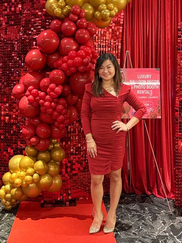 Woman in red dress posing by red and gold balloon decor at event.
