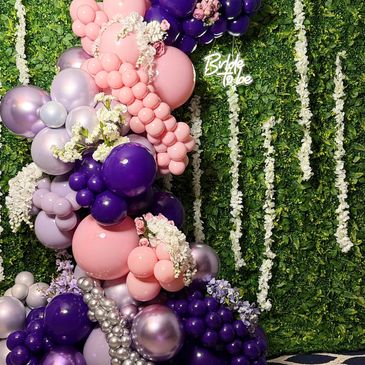 Colorful balloon arrangement with flowers and a 'Bride to be' sign on a green leafy backdrop.