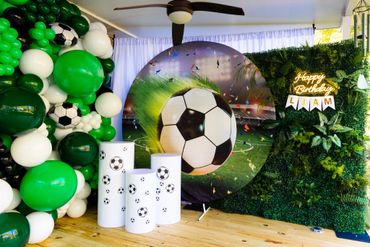 Soccer-themed birthday party setup with green and white balloons and a large soccer ball backdrop.
